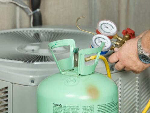 HVAC technician connecting refrigerant gauges and a refrigerant cylinder to an outdoor air conditioning unit.